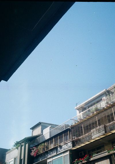 A photo looking up at the blue sky, with the upper floor balaconies of an apartment building visible in the lower half of the shot. 