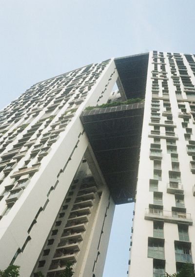 Looking up at a high rise residential building. The buildings are connected by walkways & parks on some of the upper floors.