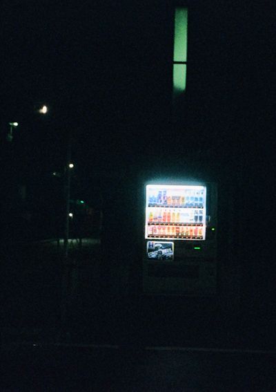 A brightly lit vending machine sits off center in an otherwise dark frame.