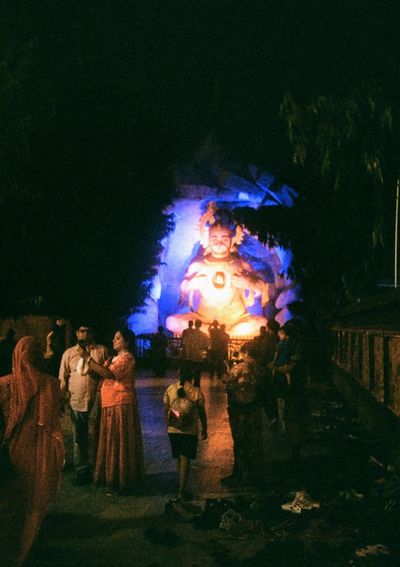 A half-monkey, half-man god statue is brightly lit at night while worshippers take selfies in front of it.