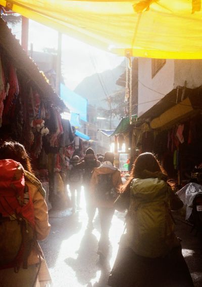 People dressed in warm winter hiking gear with backpacks walk through a market towards the morning sun.