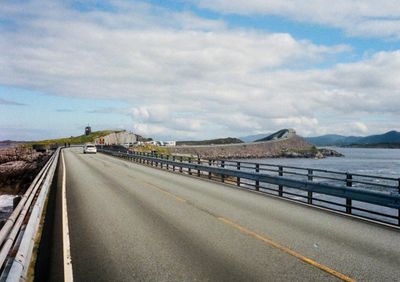 Looking down a two-lane highway road that turns right towards a bridge which arches towards the sky.