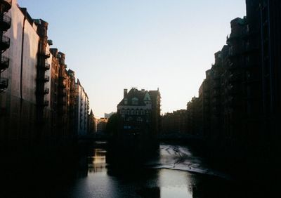 A building sits between two canals that branch off. The scene is dark, with only the sunset in the background illuminating part of the shot.