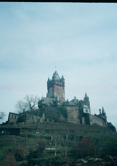 An old, stone castle sits atop a tree covered hill.