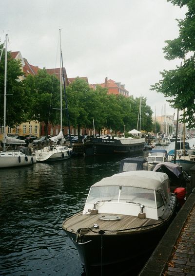 Houseboats line a canal, parked under green trees.