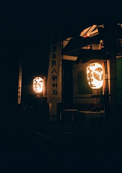 Two bright orange lanterns hang illuminated at the entrance of a temple at night.