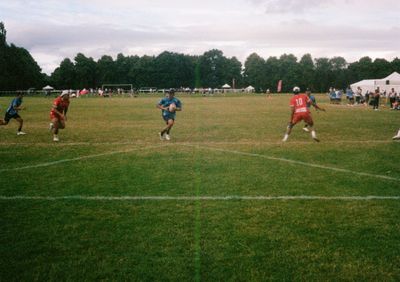 A Japanese player wearing a blue shirt runs through a gap between two Tongan players in red. He holds the ball in two hands, looking for a teammate to pass to.