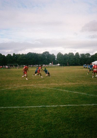 A player wearing a blue Japanese shirt leans in to touch a Tongan defender. The Japanese player is holding a rugby ball in one hand, ready to place it on the ground after the touch.