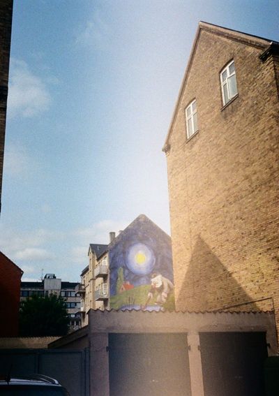 A mural of a man leaning over a lake under a full moon is painted on the side of an apartment. The buildings around it all have a monotone dull brick colour, making the mural stand out.