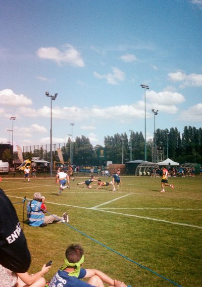 A boy dives forward with one hand holding a rugby ball. Two defenders in blue Scotland shirts reach down to try and touch him.