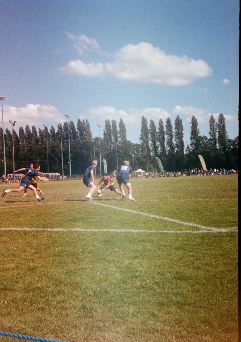 A boy dives forward with one hand holding a rugby ball. Two defenders in blue Scotland shirts reach down to try and touch him.