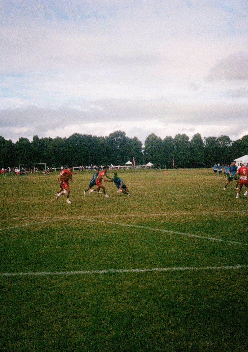 A player wearing a blue Japanese shirt leans in to touch a Tongan defender. The Japanese player is holding a rugby ball in one hand, ready to place it on the ground after the touch.