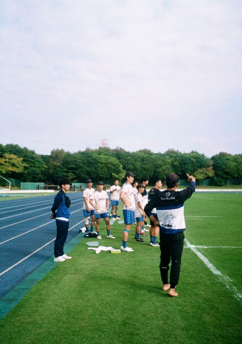 A group of players stand on the sideline, watching the team play on the field.