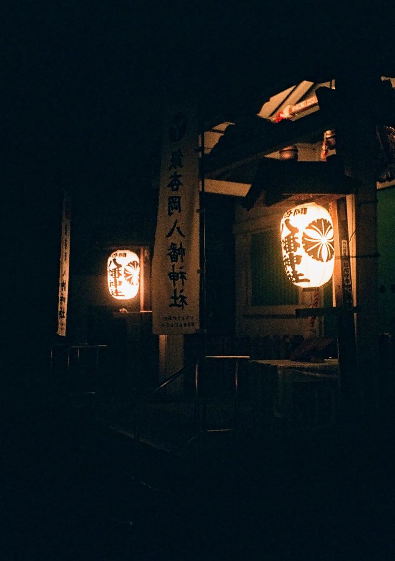 Two bright orange lanterns hang illuminated at the entrance of a temple at night.