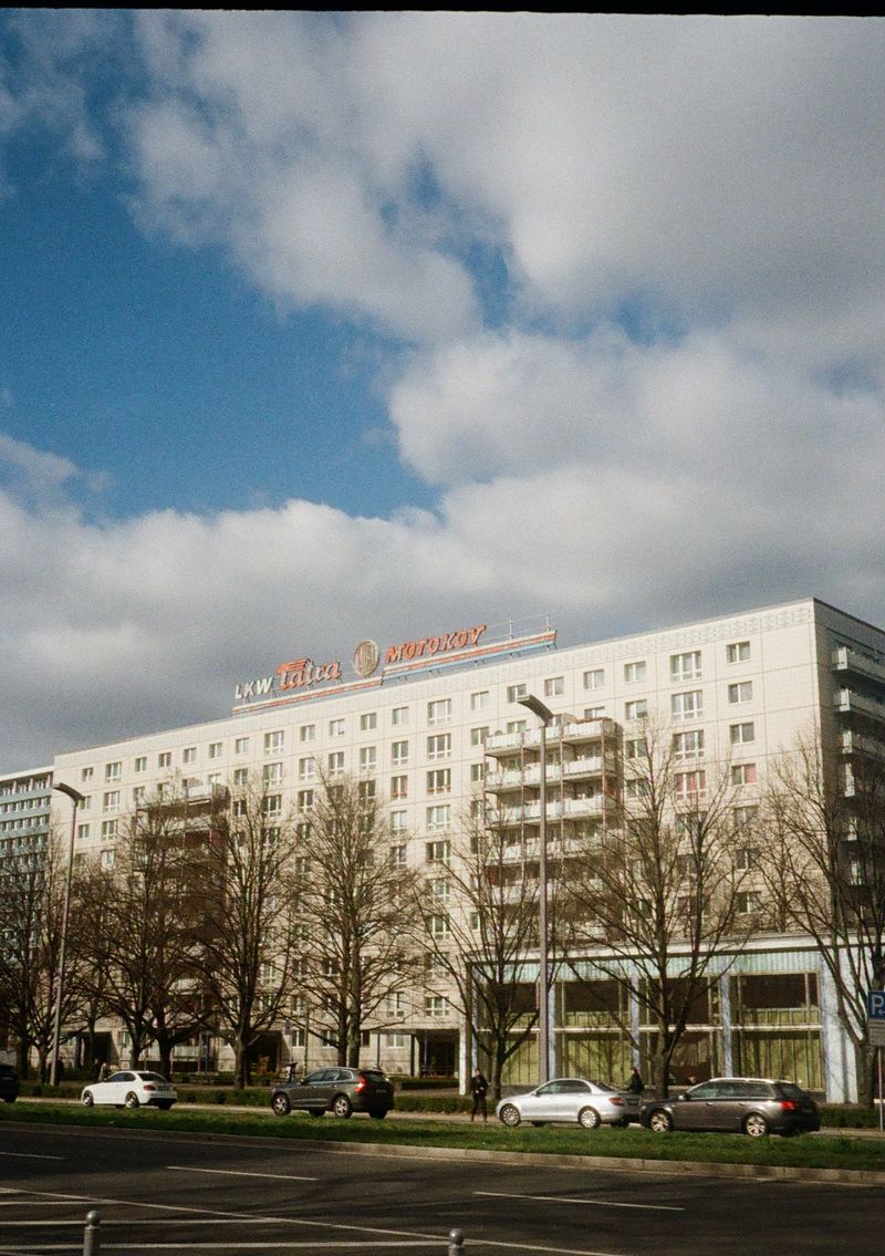 An old soviet-style apartment building sits across the road behind some leafless trees.