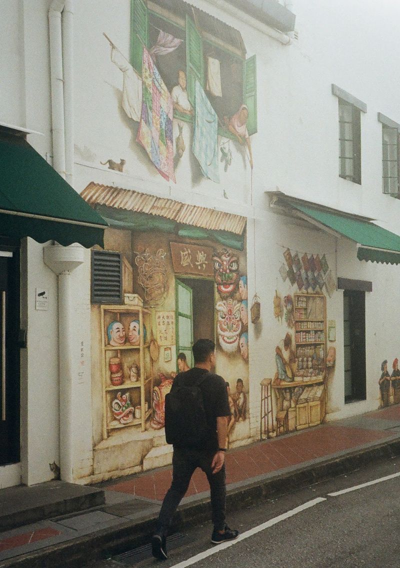 A man wearing all black and carrying a black backpack walks by a mural showing a street stall, painted on a white building