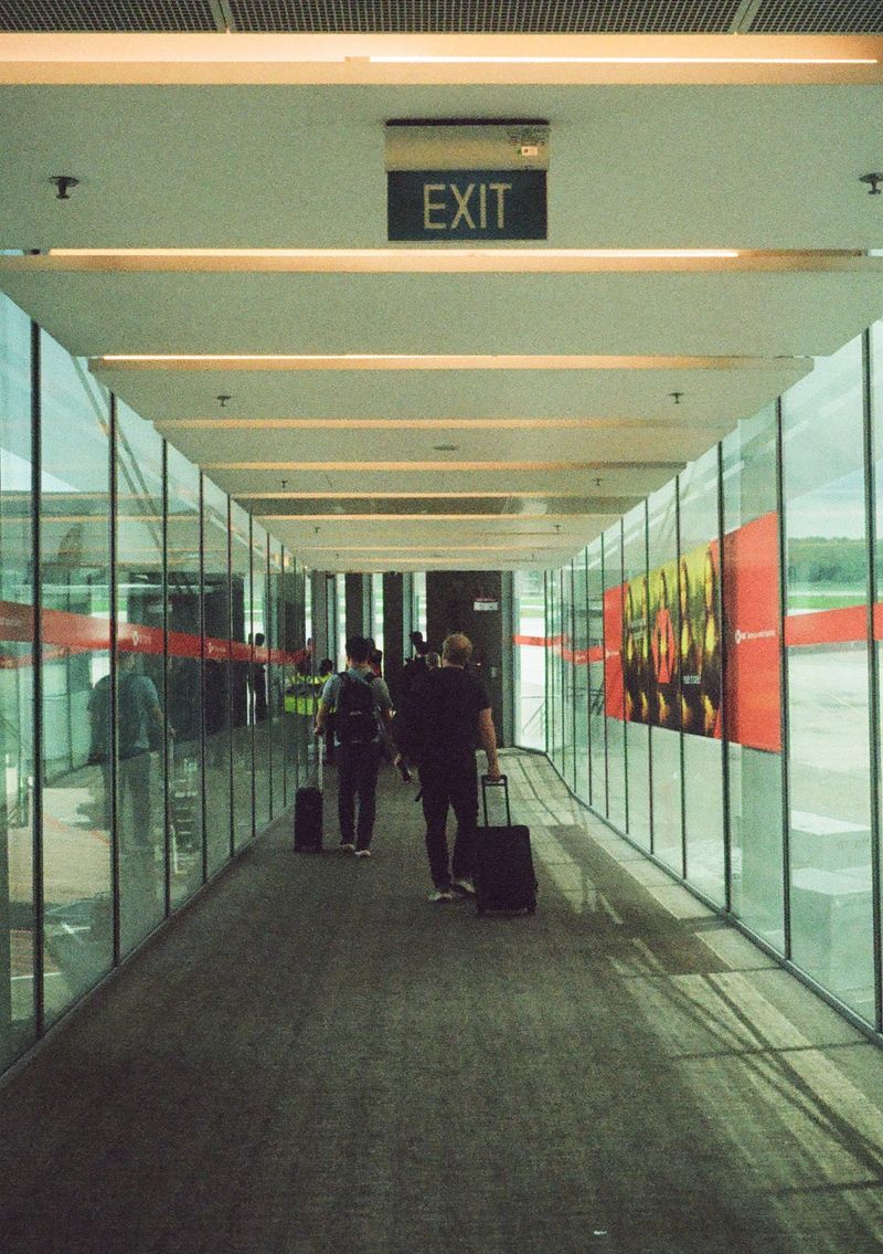 A man wheels his suitcase down an air bridge, preparing to board a plane. A sign at the top of the frame reads 'exit'.