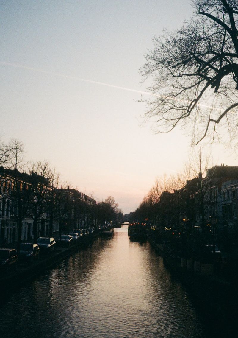 Looking down a canal lined by brick houses. The canal is reflecting the later afternoon sunset .