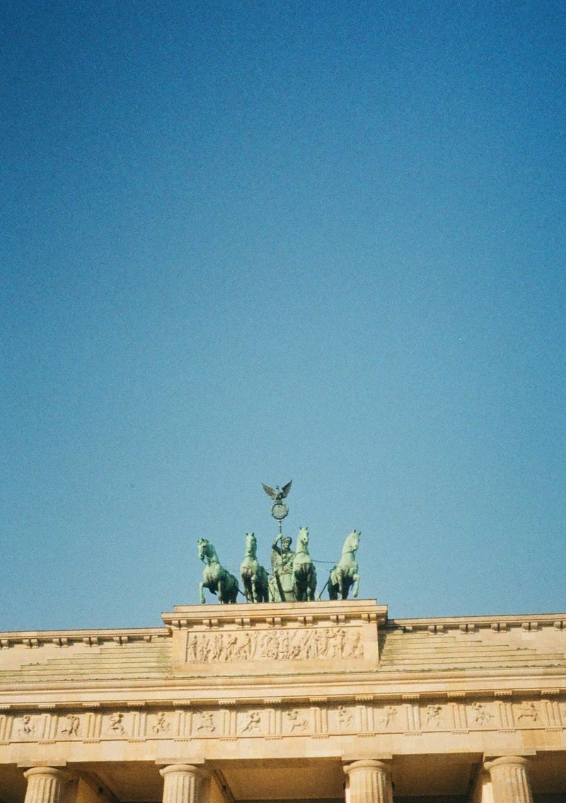 A goddess riding a horse-drawn chariot sits on top of a stone foundation. The shot looks upwards towards the subject, with the top two-thirds of the picture taken up by a clear blue sky.