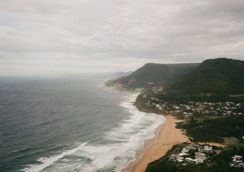 Looking down at coastal cliffs. A beach is in the foreground, with tree covered cliffs in the backgound. The sea is to the left of the shot.