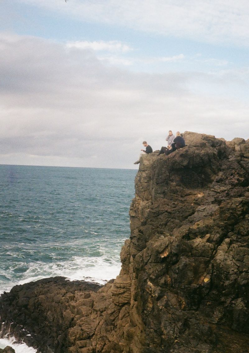 A group of people sit on a rock outcrop looking out over the Tasman Sea.