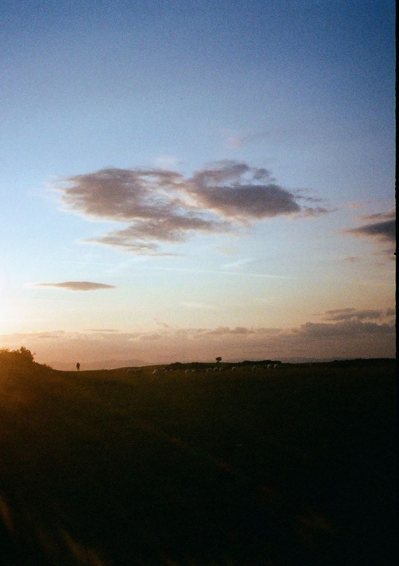 The figure of a man is in the distance, walking away from the camera as the sunsets to his left.