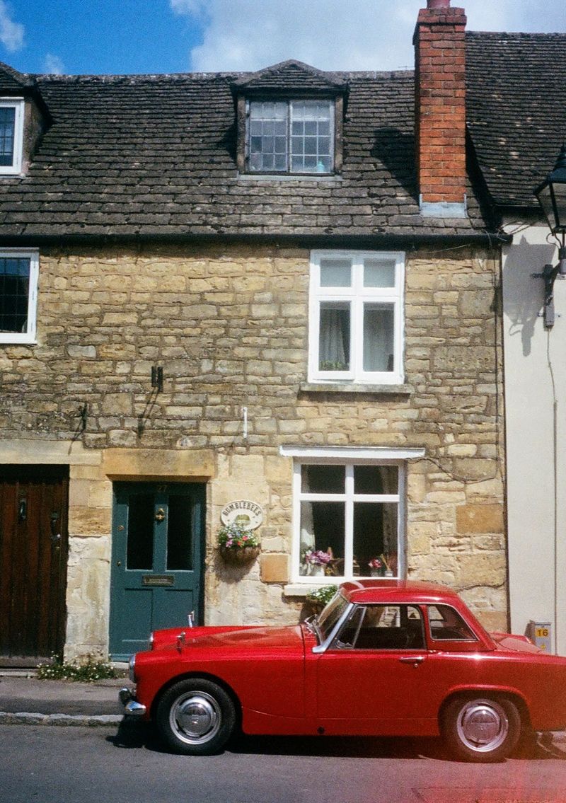 A red sports car is parked in front of an old stone brick house.