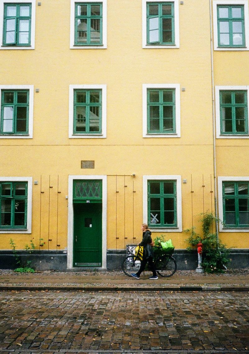 A woman walks her bicycle against the backdrop of a bright yellow building.