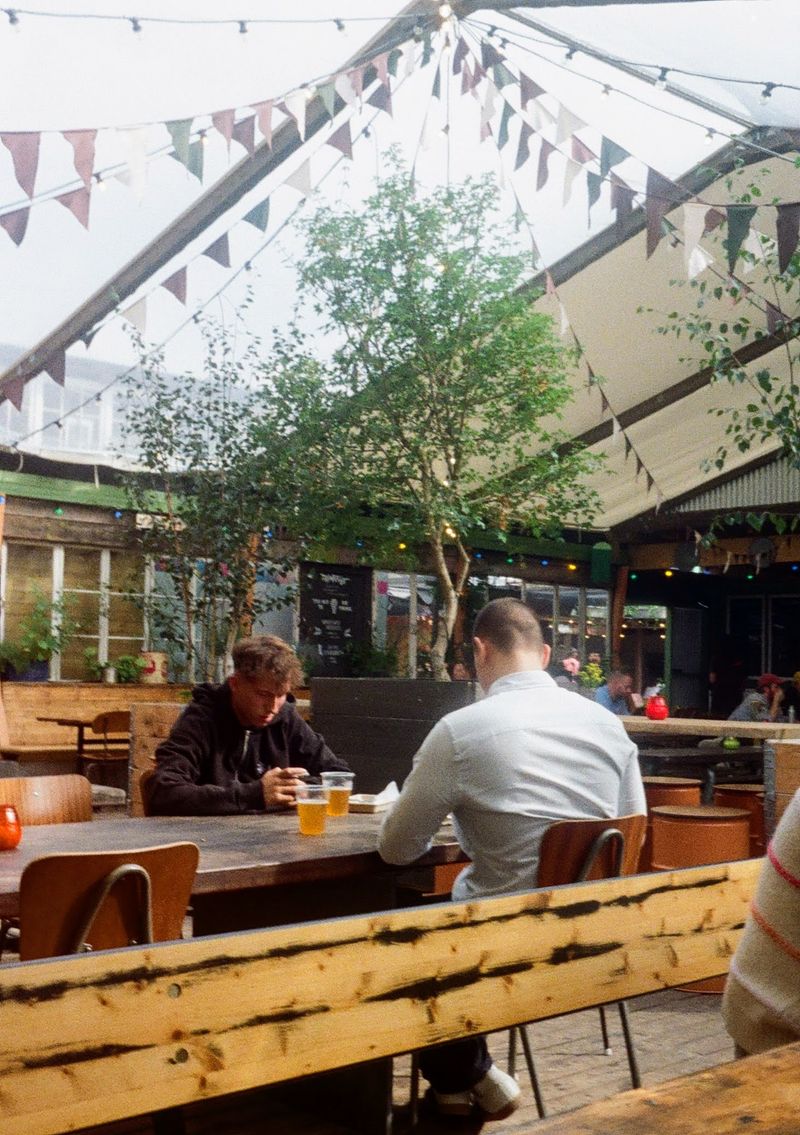 Two men sit at a table with a beverage each. The roof overhead lets in plenty of natural light.