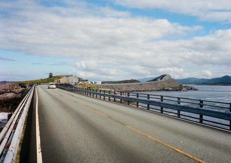 Looking down a two-lane highway road that turns right towards a bridge which arches towards the sky.