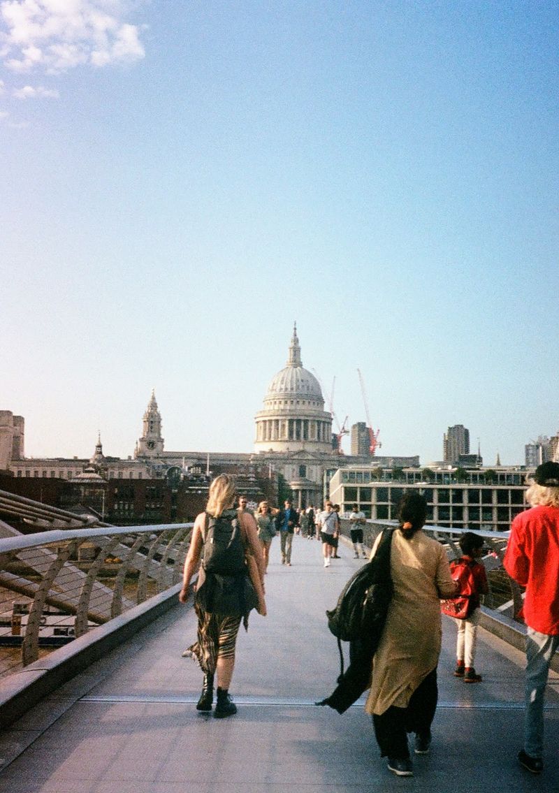 People walking on a bridge, with the white domed roof of St Paul's Cathedral in the background.