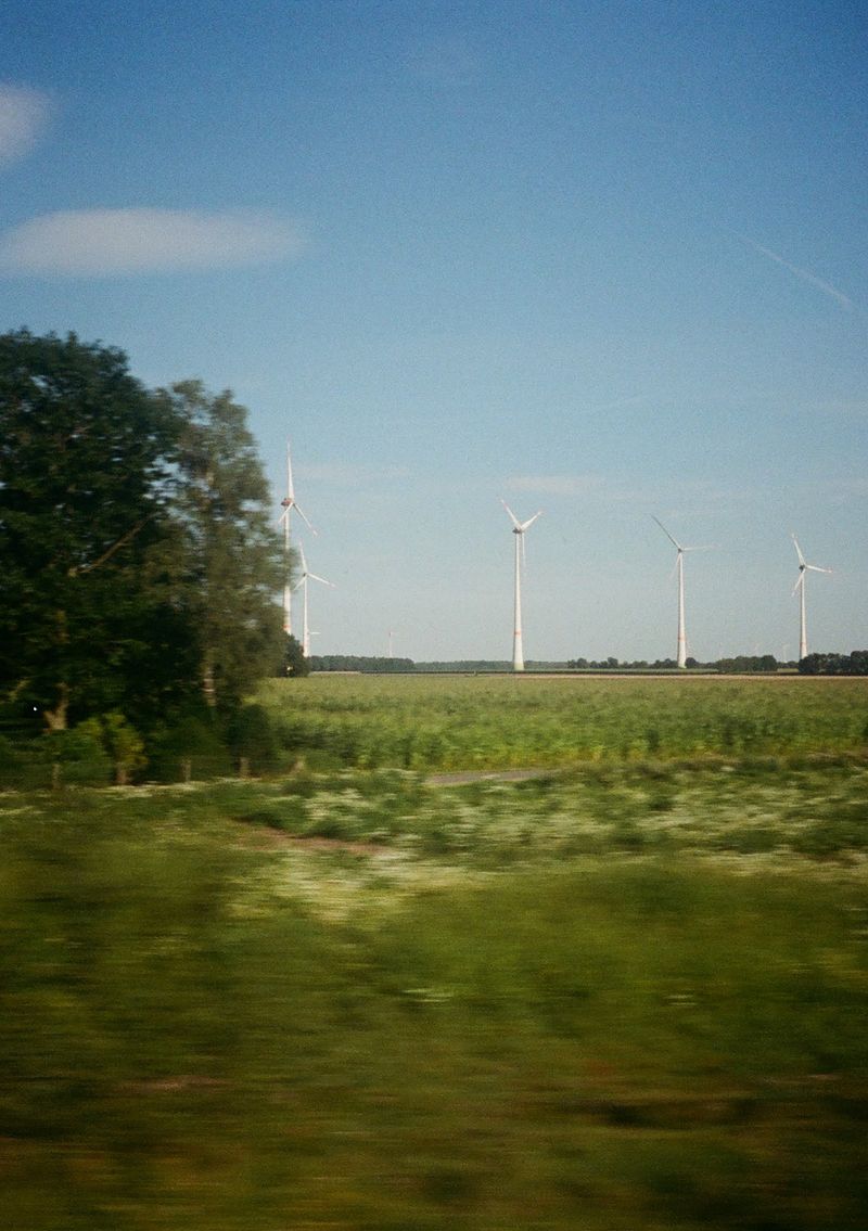 Wind turbines spinning in the distance, in a green field. Taken from a moving train.