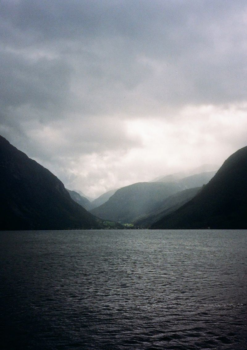 A photo taken from a ferry, looking over the water towards a valley with mountains on either side folding away into the distance. Some light rain gives the distant town and mountains a misty coating.