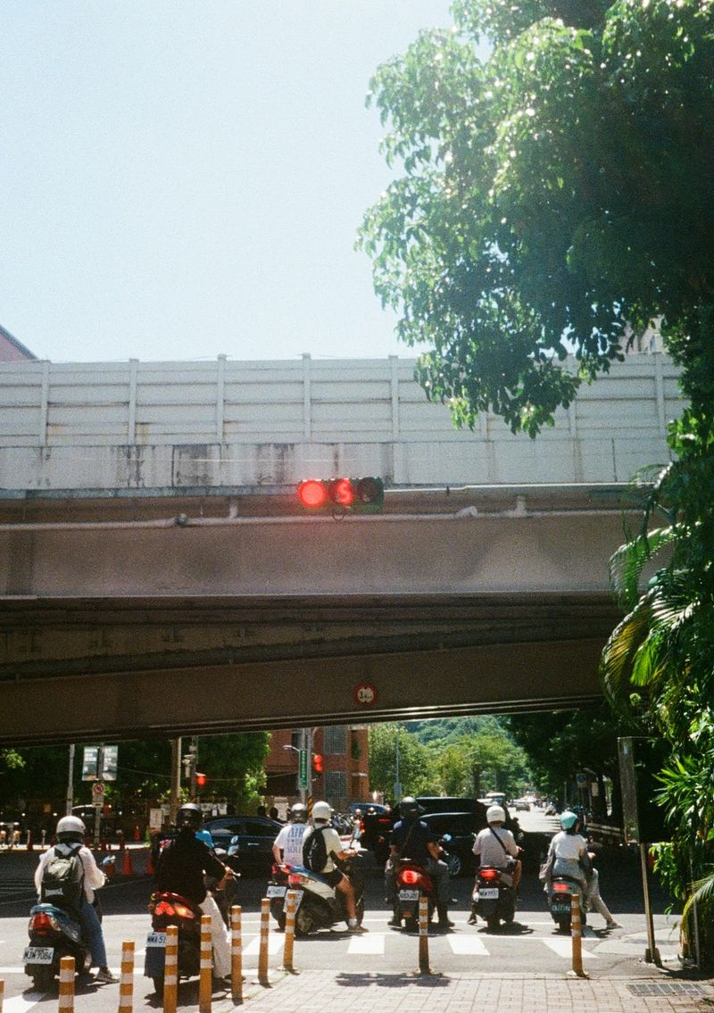 Scooters waiting at a red light with 5 seconds showing on the countdown. They are ready to go under an overpass.