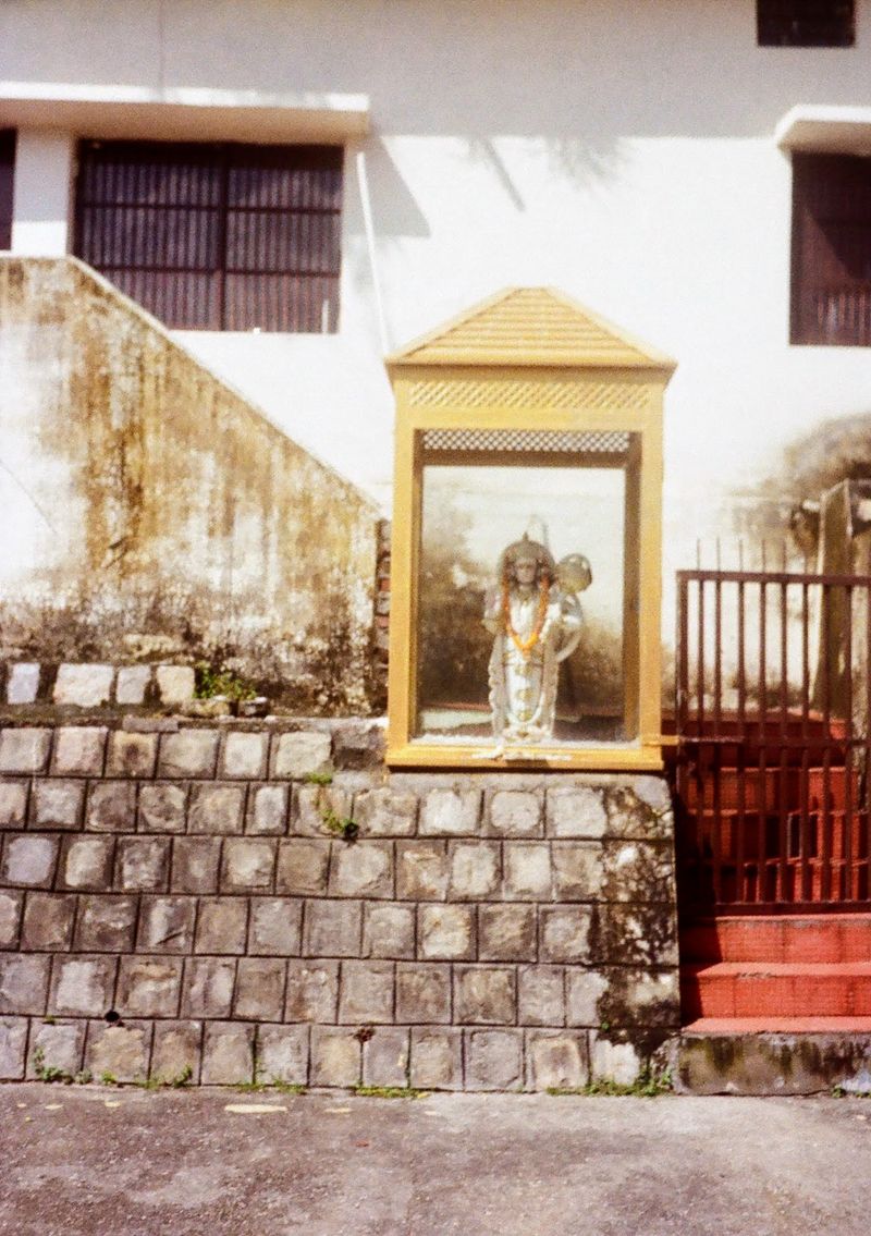 A white statue of a Hindu deity sit in a golden glass encased box next to a red gated staircase.