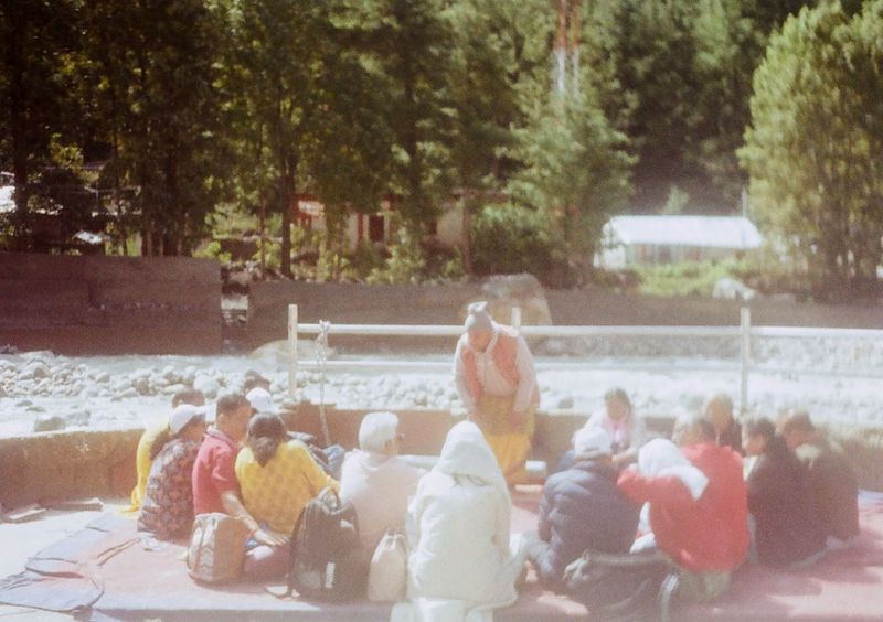 Worshipers sit in a circle while a priest conducts a religious ceremony on the banks of a river.