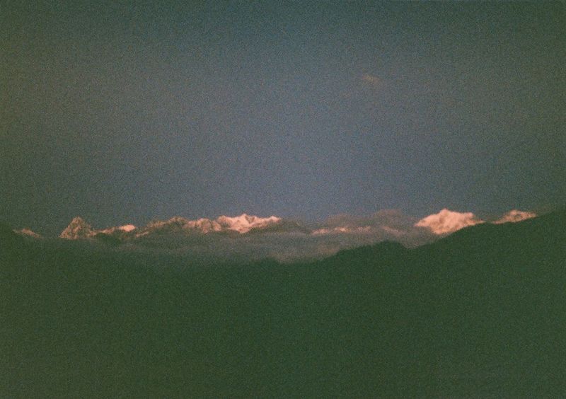 A ridge of snow capped mountain peaks with the last bits of light casting a pinkish hue on their tops.