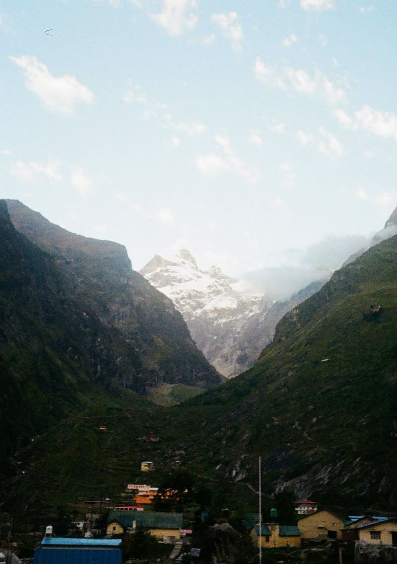 A snow capped mountain rises up between two hills.