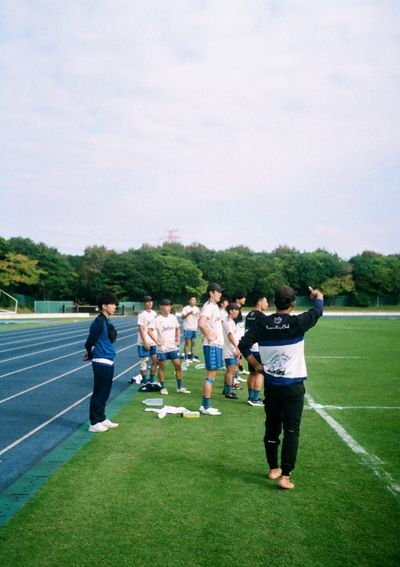 A group of players stand on the sideline, watching the team play on the field.