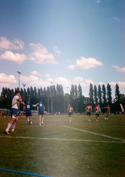 A referee wearing white points to the mark while awarding a try. They are holding their whistle to their mouth, their cheeks puffed. Players from both teams walk away, backs turned to the camera.