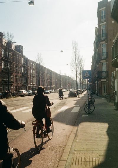 A person riding a bicycle in the midday sunlight rides away from the camera.