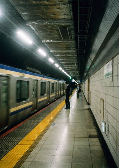 A man waits on the platform as a train pulls into the station in front of him. The man is dressed in a black suit and pants.