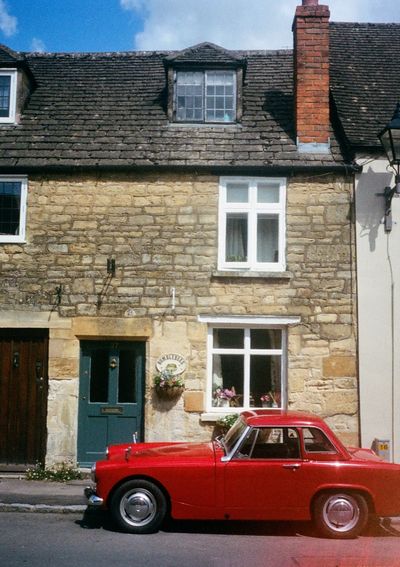 A red sports car is parked in front of an old stone brick house.